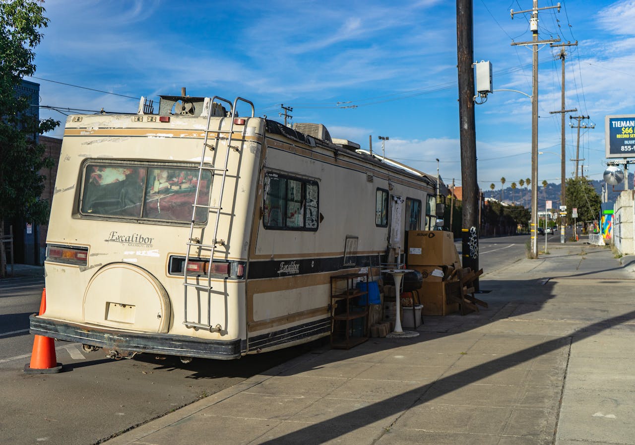 home-hero-1 A vintage Excalibur RV parked on an urban street with scattered items outside.