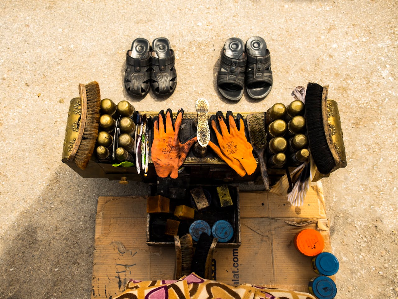 services-03 Aerial view of a shoe shine setup with brushes, polish, gloves, and sandals on a concrete surface.